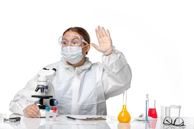 Front view female doctor in special suit and wearing mask using microscope on light-white background covid- virus pandemic coronavirus