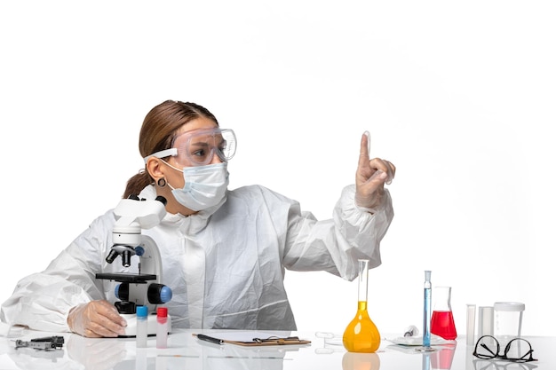 Front view female doctor in special suit and wearing mask using microscope on light white background covid- virus pandemic coronavirus