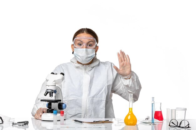 특수 양복에 전면보기 여성 의사와 현미경을 사용하여 마스크를 쓰고 흰색 배경 covid-virus pandemic coronavirus 작업