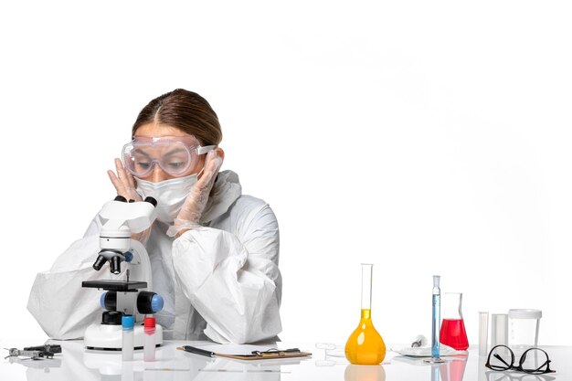 Front view female doctor in special suit and wearing mask working with microscope on white desk covid- virus pandemic coronavirus