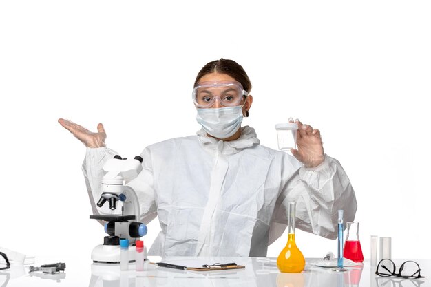 특수 양복과 밝은 흰색 배경에 빈 플라스크를 들고 마스크가있는 전면보기 여성 의사 covid- pandemic health coronavirus virus