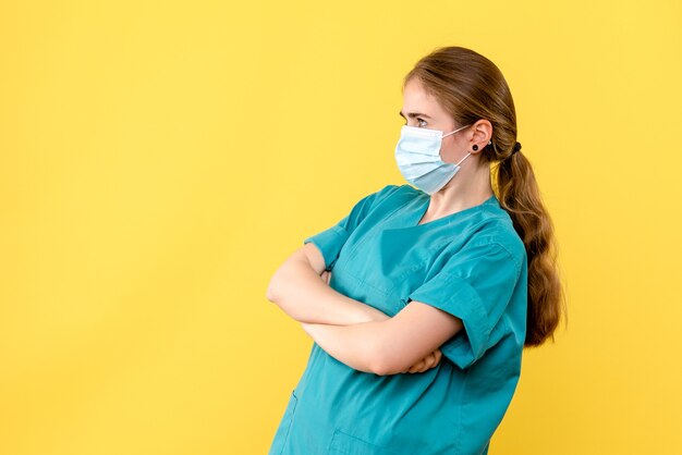 Front view female doctor in sterile mask on yellow background pandemic health virus covid