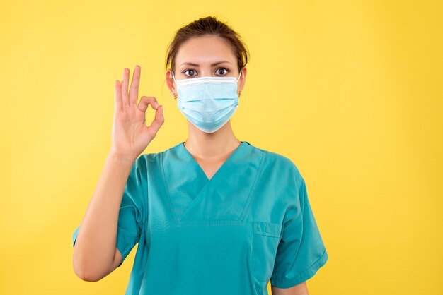 Вид спереди женщина-врач в стерильной маске на желтом фоне