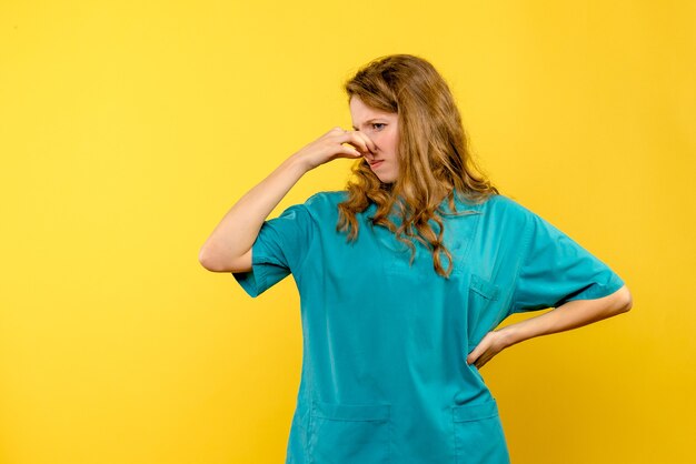 노란색 벽에 여성 의사 stucking 코의 전면보기