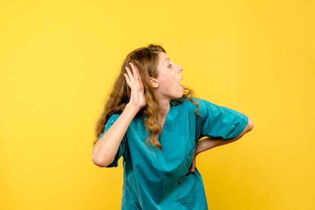 Front view of female doctor trying to listen on yellow wall