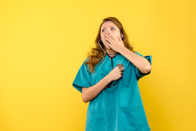 Front view female doctor using stethoscope on yellow space