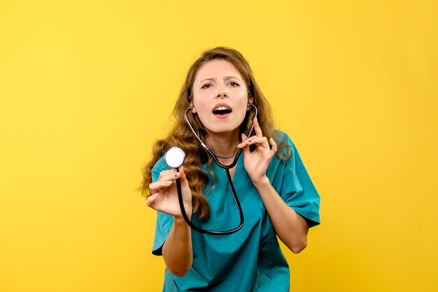 Front view of female doctor using stethoscope on yellow wall