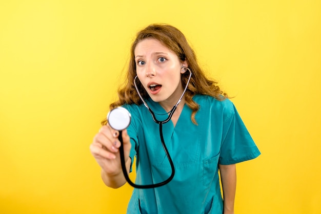 Front view of female doctor using stethoscope on yellow wall
