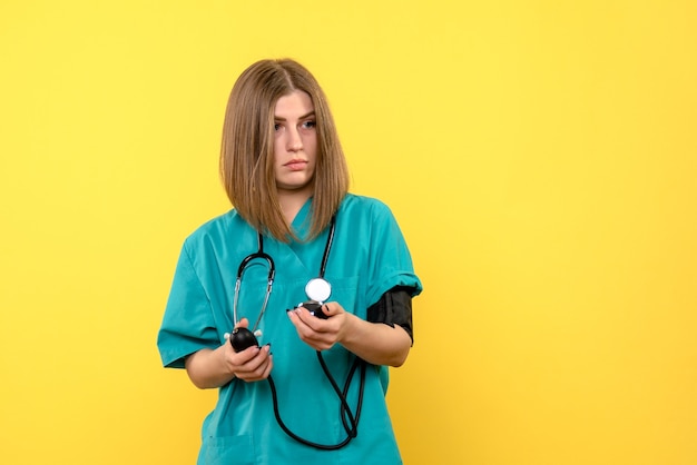 Front view female doctor using tonometer on a yellow space