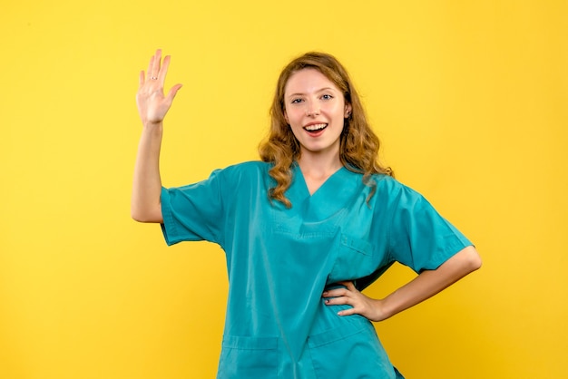 Front view of female doctor waving on yellow wall