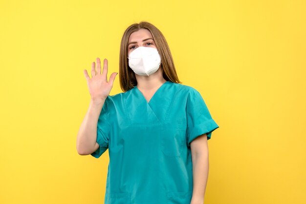 黄色い床の医療病院パンデミックウイルスのマスクを身に着けている正面図の女性医師
