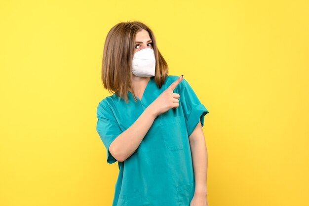 노란색 공간에 마스크를 쓰고 전면보기 여성 의사