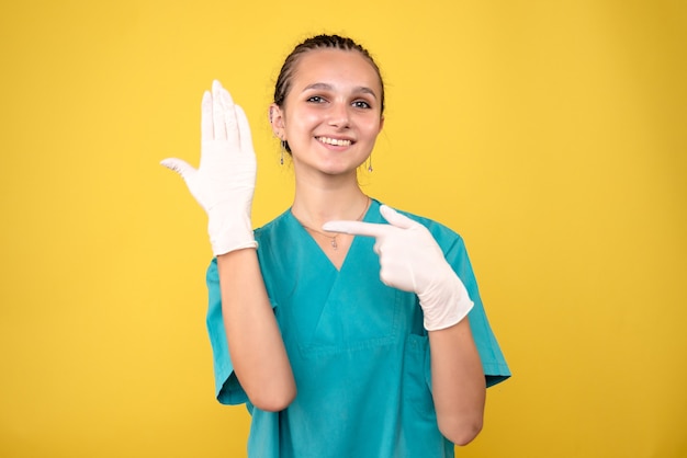 Front view of female doctor wearing special gloves on yellow wall