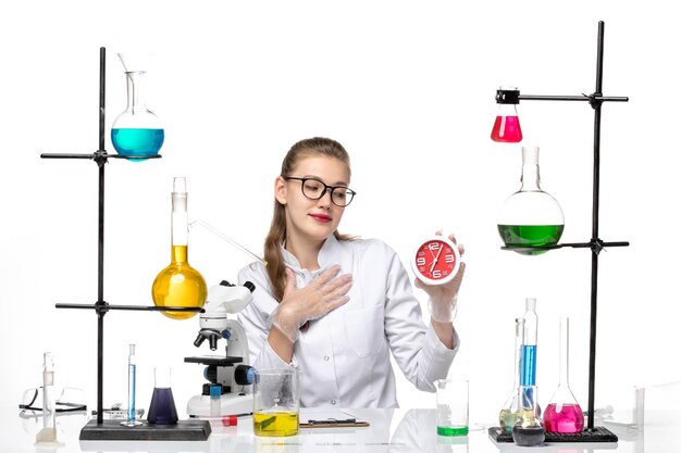 front view female doctor in white medical suit holding clocks sitting on white background virus chemistry pandemic covid