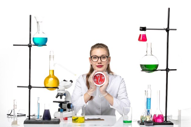 Front view female doctor in white medical suit holding clocks and smiling on white background virus covid chemistry pandemic