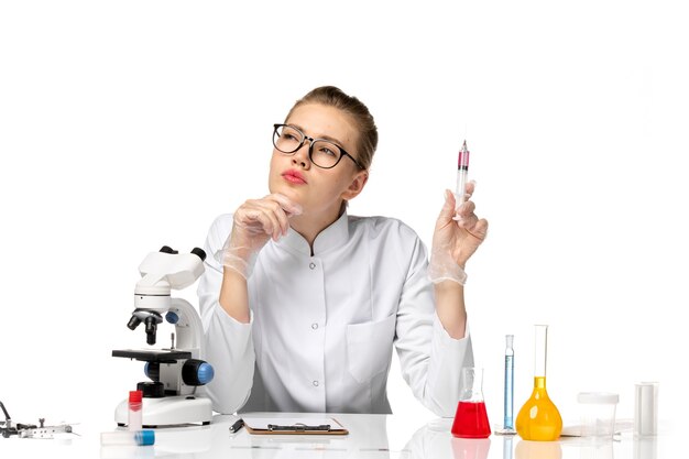 Front view female doctor in white medical suit holding injection and thinking on a white space