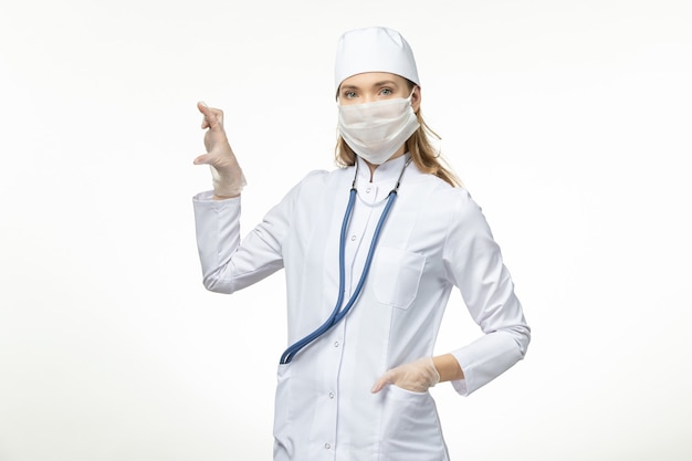 Front view female doctor in white medical suit and mask as protection from coronavirus on white wall illness covid- pandemic