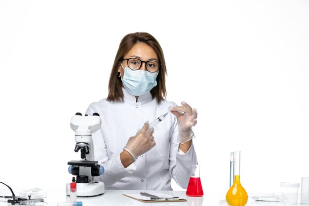 흰색 공간에 주사를 들고 코로나 바이러스로 인해 흰색 의료 양복과 마스크의 전면보기 여성 의사