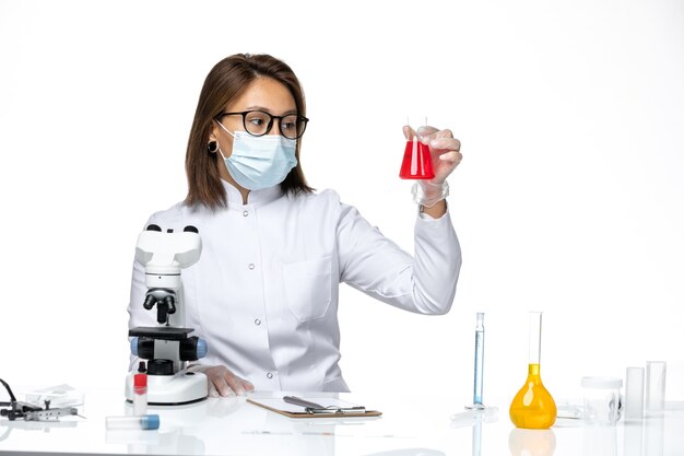 Вид спереди женщина-врач в белом медицинском костюме и маске из-за коронавируса сидит с растворами на белом пространстве