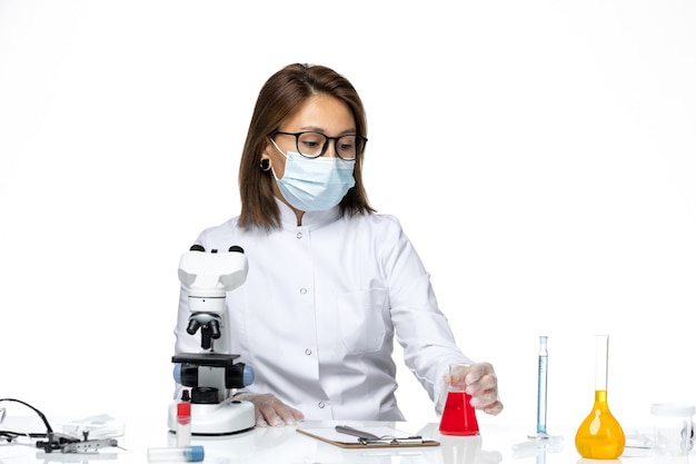 흰색 공간에 솔루션과 함께 앉아 코로나 바이러스로 인해 흰색 의료 양복과 마스크에 전면보기 여성 의사