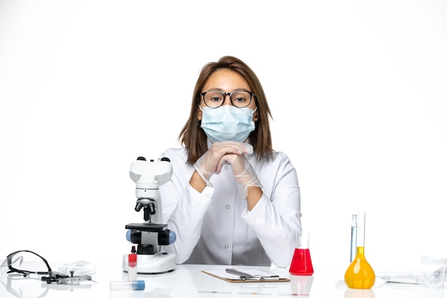 Вид спереди женщина-врач в белом медицинском костюме и маске из-за коронавируса сидит с растворами на белом пространстве
