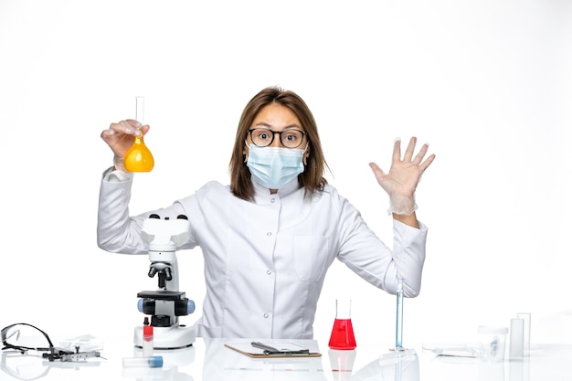 흰색 책상에 솔루션 작업 코로나 바이러스로 인해 흰색 의료 양복과 마스크의 전면보기 여성 의사