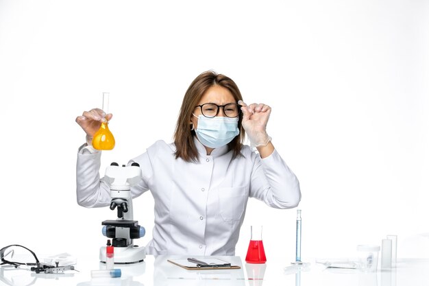 Вид спереди женщина-врач в белом медицинском костюме и маске из-за коронавируса, работающая с растворами на белом пространстве