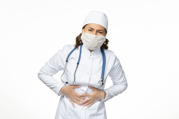 白い壁のパンデミックウイルス病の病気の薬に胃痛を持っている白い医療スーツとマスクの正面図女性医師