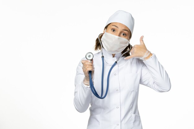 白い机の上の聴診器を使用して白い医療スーツとマスクの正面図女性医師パンデミック病医学ウイルス分離