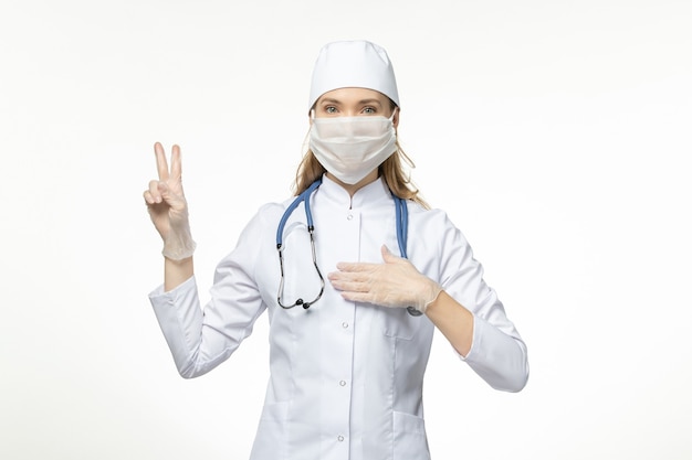 Front view female doctor in white medical suit and mask on white wall illness covid- pandemic disease