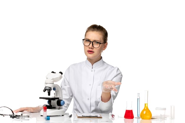 Вид спереди женщина-врач в белом медицинском костюме, сидящая перед столом с решениями на белом пространстве