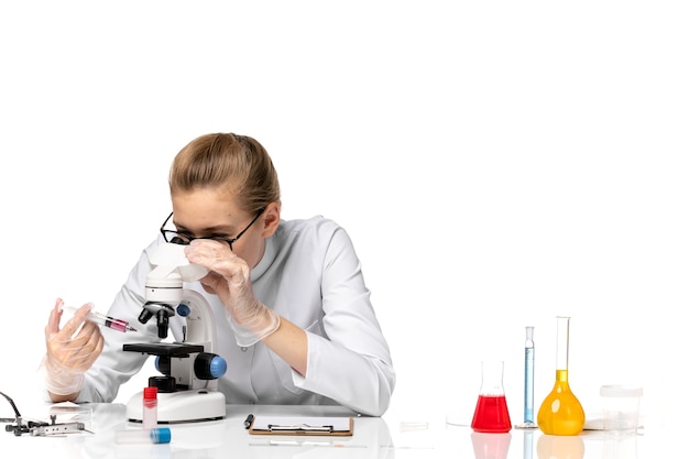 Front view female doctor in white medical suit using microscope on light white space