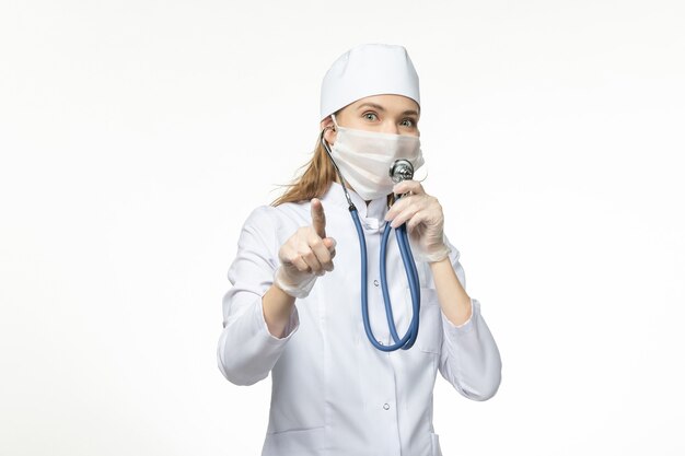 Front view female doctor in white medical suit using stethoscope on white wall illness covid- pandemic disease