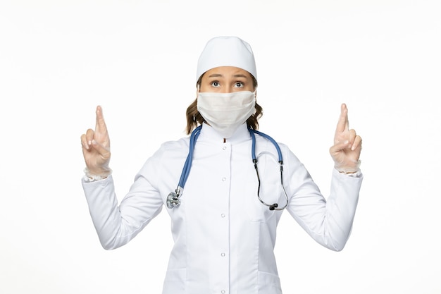 빛 벽 유행성 질병 바이러스 격리에 코로나 바이러스로 인해 마스크를 쓰고 흰색 의료 정장에 전면보기 여성 의사