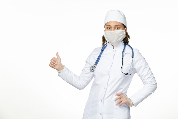 明るい白い机の上のコロナウイルスによるマスクを身に着けている白い医療スーツの正面図女性医師パンデミック病ウイルス分離