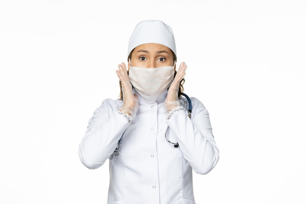 Front view female doctor in white medical suit and wearing mask due to coronavirus on light-white wall pandemic disease isolation covid