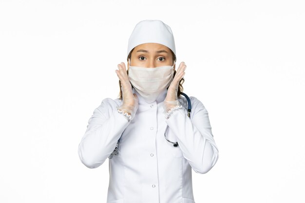흰색 의료 복을 입은 여성 의사와 밝은 흰색 벽에 코로나 바이러스로 인한 마스크 착용 전면보기 대유행 질병 격리 COVID