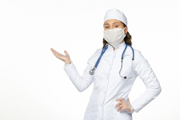 Front view female doctor in white medical suit wearing mask due to coronavirus on light white wall pandemic disease isolation