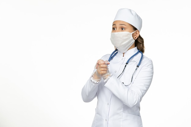 밝은 흰색 벽 유행성 질병 바이러스 격리에 코로나 바이러스로 인해 마스크를 쓰고 흰색 의료 정장에 전면보기 여성 의사