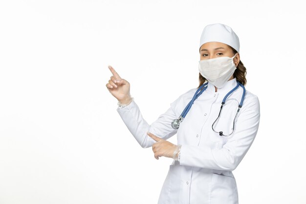 Front view female doctor in white medical suit wearing mask due to coronavirus on white desk pandemic disease isolation