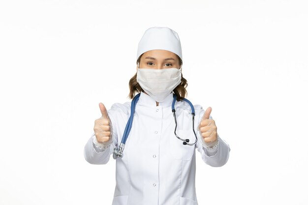 Front view female doctor in white medical suit and wearing mask due to coronavirus on the white desk pandemic virus disease isolation covid