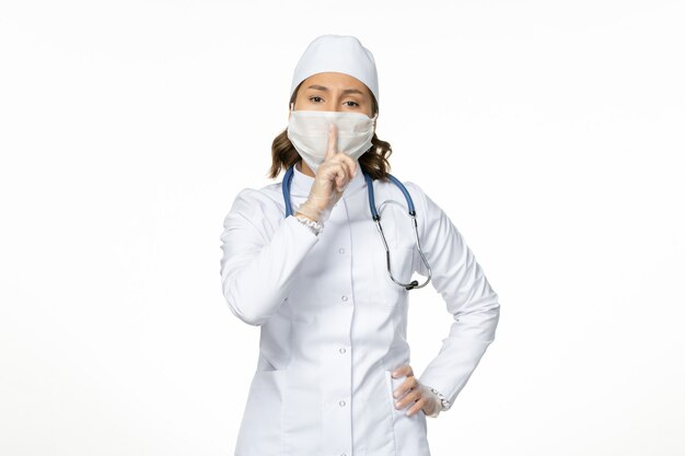 Вид спереди женщина-врач в белом медицинском костюме и в маске из-за коронавируса на белом полу изоляция пандемической болезни covid