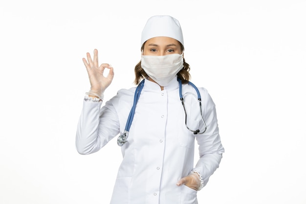 Front view female doctor in white medical suit and wearing mask due to coronavirus on the white floor pandemic virus disease isolation covid