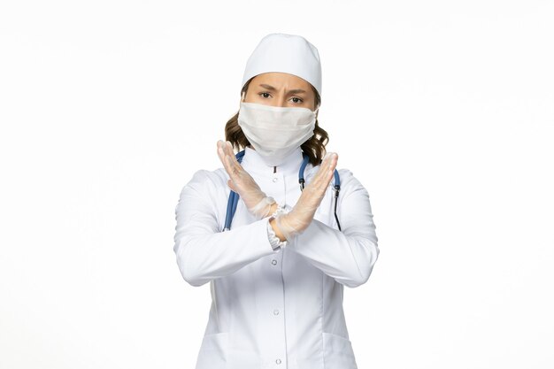 白い医療スーツと白い壁のパンデミック病隔離covidのコロナウイルスによるマスクを身に着けている正面図の女性医師