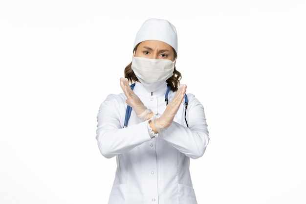 Front view female doctor in white medical suit and wearing mask due to coronavirus on white wall pandemic disease isolation covid