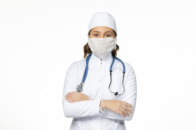Front view female doctor in white medical suit wearing mask due to coronavirus on white wall pandemic disease virus isolation