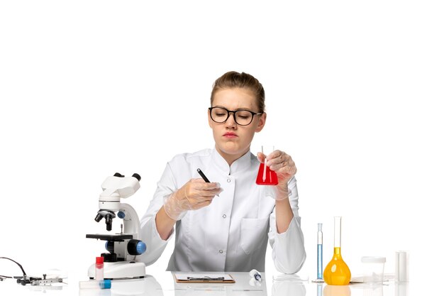 Front view female doctor in white medical suit with gloves holding flask with solution on a light white space