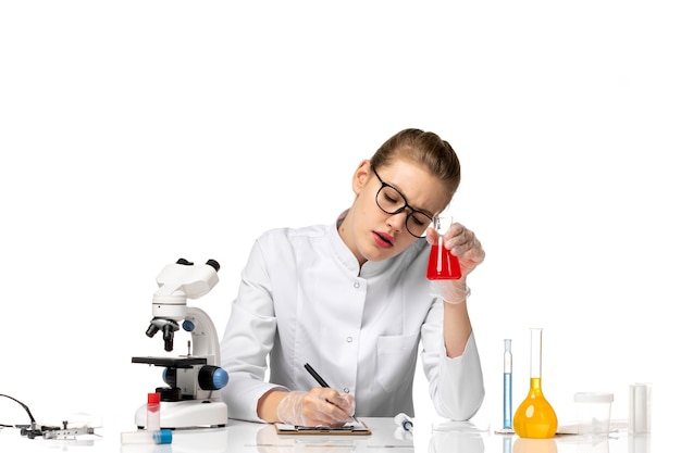 Front view female doctor in white medical suit with gloves holding flask with solution on a white floor health pandemic covid- disease