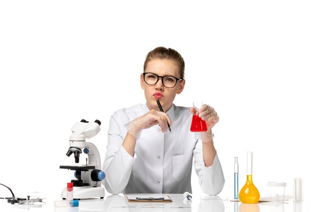 Front view female doctor in white medical suit with gloves holding flask with solution on a white space