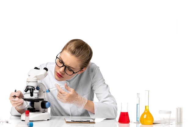 Front view female doctor in white medical suit with gloves holding injection on the white desk